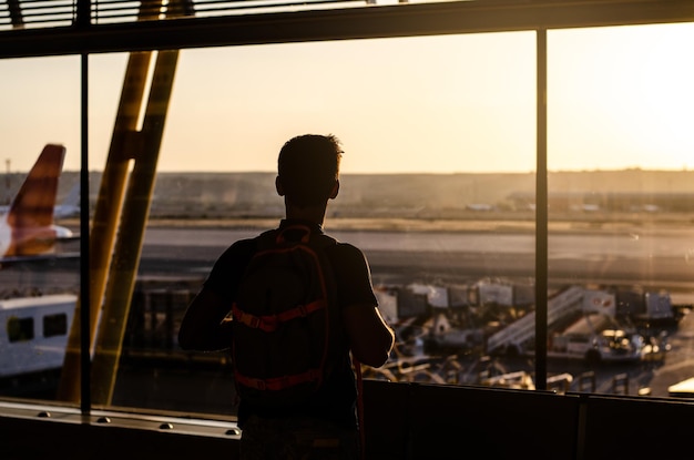 Nachdenklicher junger Mann, der durch das Fenster auf ein Flughafenterminal blickt