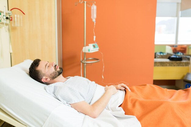 Nachdenklicher kranker Patient mit Sauerstoff, der während der Behandlung auf dem Krankenhausbett liegt