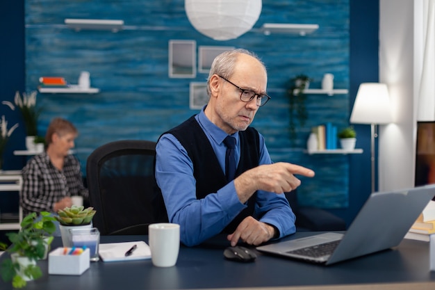 Nachdenklicher leitender geschäftsmann, der auf laptop zeigt, während er von zu hause aus arbeitet, älterer unternehmer ...