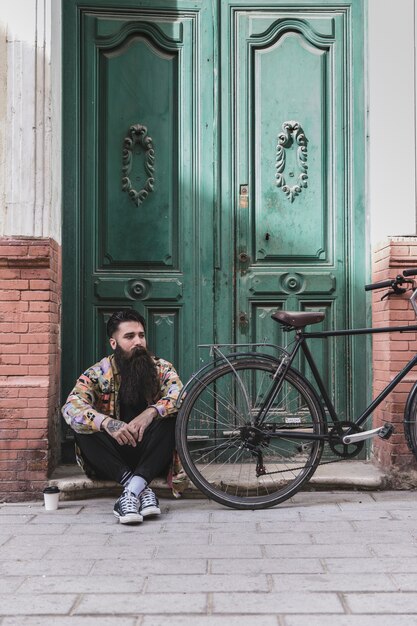 Nachdenklicher Mann, der vor alter Tür mit seinem Fahrrad sitzt