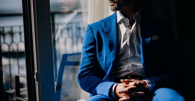 Nachdenklicher Mann im blauen Anzug sitzt auf dem Fensterbrett