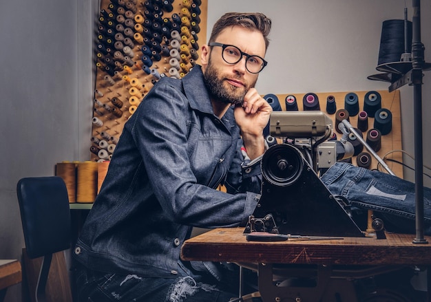 Kostenloses Foto nachdenklicher schneider, der in einer nähwerkstatt mit der hand am kinn am tisch sitzt.