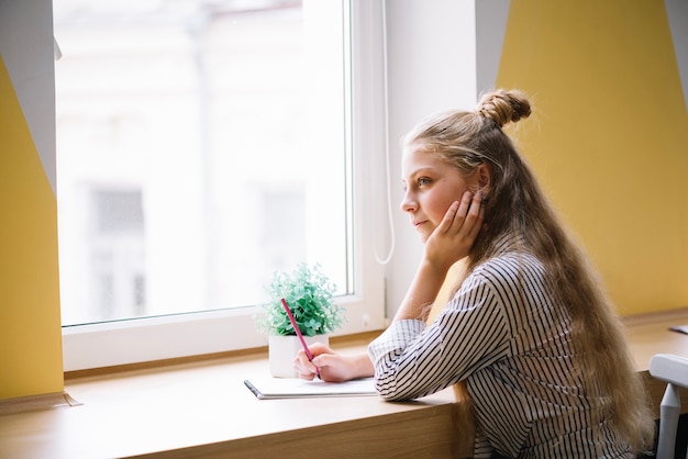 Nachdenklicher Schüler in der Nähe von Fenster mit Studien