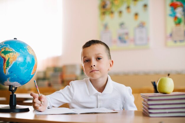 Nachdenklicher Schüler mit Globus auf dem Schreibtisch