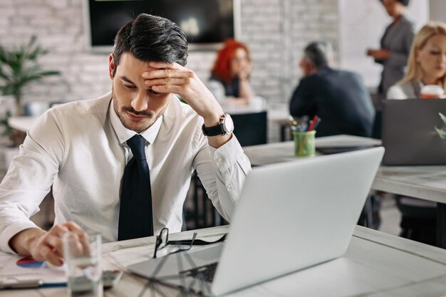 Nachdenklicher Unternehmer, der Geschäftsberichte liest, während er im Büro arbeitet. Im Hintergrund sind Menschen zu sehen