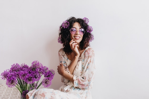 Nachdenkliches afrikanisches Mädchen mit lila Blumen, die weg schauen. Innenaufnahme der schwarzen Debonair-Dame isoliert.