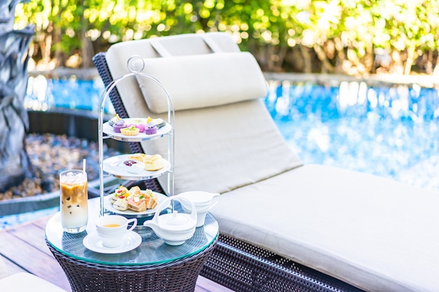 Nachmittagstee-Set mit Latte-Kaffee und heißem Tee auf dem Tisch in der Nähe des Stuhls um den Pool