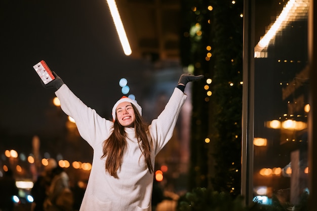 Nachtstraßenporträt der jungen schönen Frau, die begeistert wirkt. Festliche Girlandenlichter.