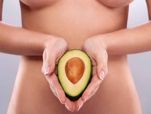 Nackte Frau hält die frische Avocado