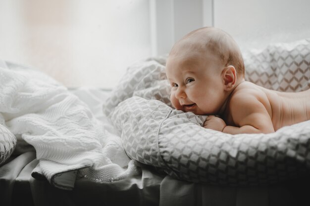 Nackter neugeborener Junge liegt auf der weichen Decke vor einem hellen Fenster