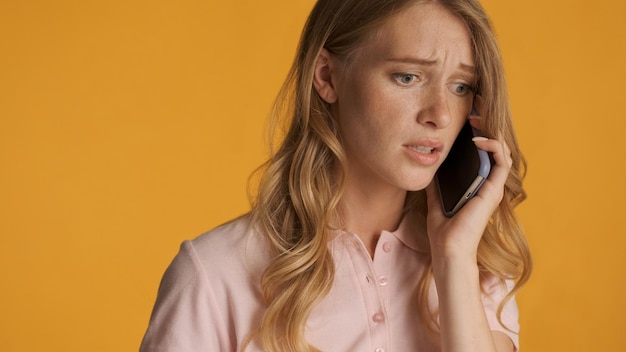 Kostenloses Foto nahaufnahme ängstliche blonde frau, die emotional am telefon spricht, isoliert auf buntem hintergrund. sorgenausdruck