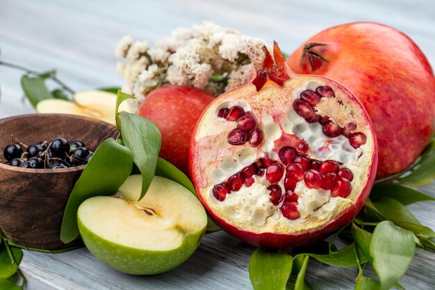 Nahaufnahme Ansicht von Früchten als Granatapfel- und Apfelhälften mit ganzen und Schale der Schlehe mit Blumen und Blättern auf schwarzer Oberfläche