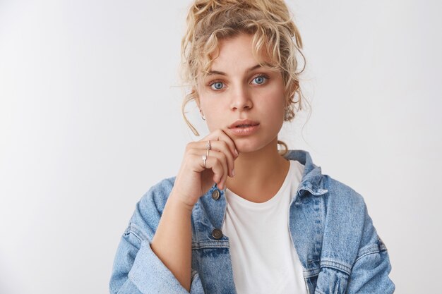 Nahaufnahme attraktive nachdenklich fokussierte faszinierte junge Studentin, die interessanten Vortrag mit offenem Mund interessiert, Blick blaue Augen Kamera zuhört, Lippe neugierig stehende weiße Wand berühren