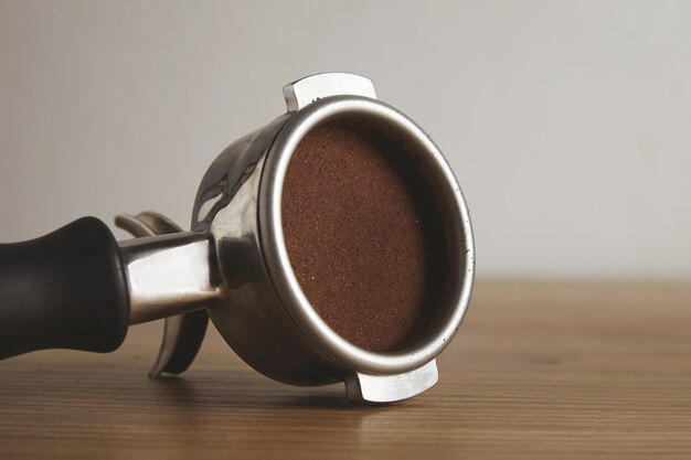Nahaufnahme auf Stahl-Siebträger mit gemahlenem Kaffeepulver nach innen gedrückt. Isoliert auf Holztisch im Caféladen. Professionelle Kaffeezubereitung