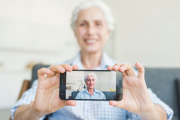 Kostenloses Foto nahaufnahme der älteren frau ihr foto auf smartphone zeigend