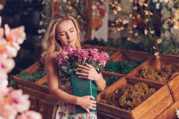 Nahaufnahme der blonden jungen Frau, die den rosa Rosentopf umfasst