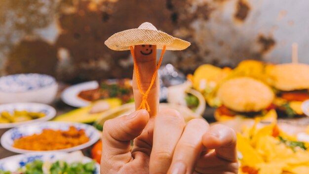 Nahaufnahme der Fingerkunst mit kleinem Hut und mexikanischem Lebensmittel am Hintergrund