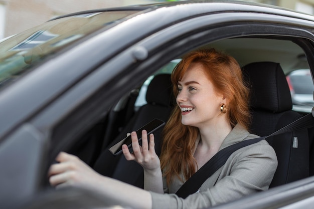 Nahaufnahme der Frau, die Handy benutzt und während der Autofahrt über den Lautsprecher spricht Frau, die während der Fahrt über die Freisprecheinrichtung im Auto spricht
