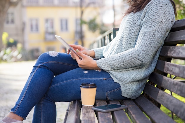 Nahaufnahme der Frau, die Tablette verwendet und draußen auf Bank sitzt