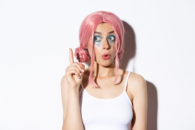 Nahaufnahme der frau in der rosa parteiperücke und im hellen make-up, haben idee, zeigefinger im eureka-zeichen erhebend, stehend.
