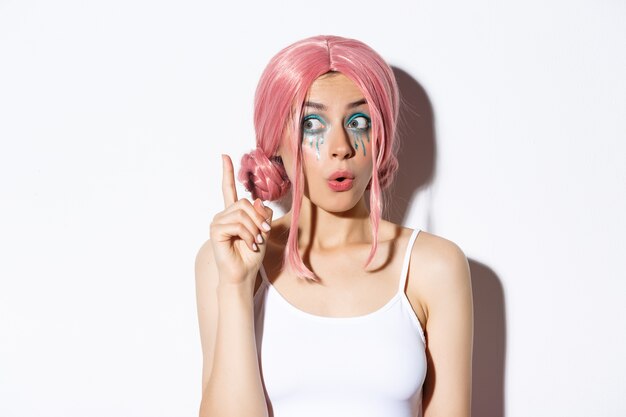 Nahaufnahme der Frau in der rosa Parteiperücke und im hellen Make-up, haben Idee, Zeigefinger im Eureka-Zeichen erhebend, stehend.