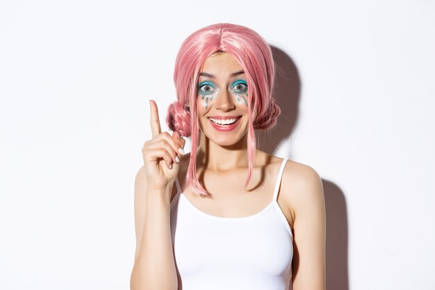 Nahaufnahme der Frau in der rosa Parteiperücke und im hellen Make-up, haben Idee, Zeigefinger im Eureka-Zeichen erhebend, stehend.