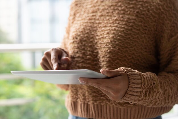 Nahaufnahme der Frau in der warmen Strickjacke unter Verwendung der Tablette auf Balkon