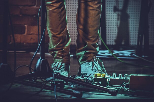 Nahaufnahme der Füße einer Person in der Nähe von Gitarrenpedalen und einem Mikrofonständer unter den Lichtern
