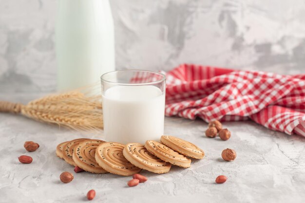 Nahaufnahme der Glasbecherflasche gefüllt mit Milch und Keksen Erdnüsse Spikes rot gestreiftes Handtuch auf gefärbtem weißem Hintergrund