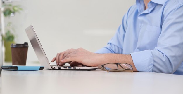 Nahaufnahme der Hände des jungen Mannes mit Laptop-Computer im Café, Restaurant oder Büro, während er Kaffee oder Tee trinkt.