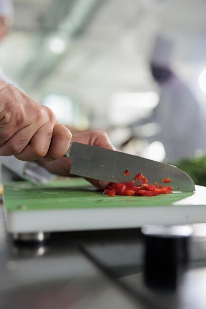 Nahaufnahme der Hände des Küchenchefs, die frische und organische rote Paprika schneiden, während sie ein Gourmetgericht für das Abendessen kochen. Gastronomieexperte schneidet Gemüse und Gemüse für eine köstliche Mahlzeit.