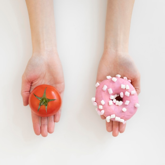 Nahaufnahme der Hände, die Donut und Tomate halten