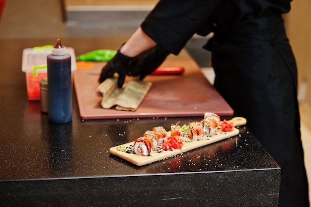 Nahaufnahme der Hände professioneller Köche in schwarzen Handschuhen, die Sushi und Brötchen in einer Restaurantküche mit traditioneller japanischer Küche zubereiten