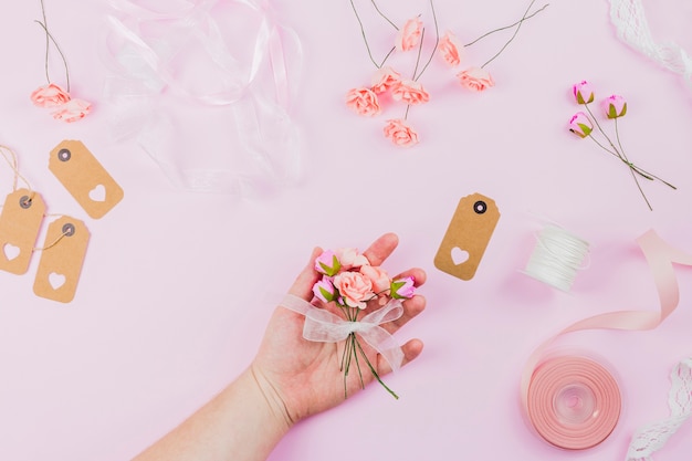 Nahaufnahme der Hand der Frau Blume halten gebunden mit weißem Band gegen rosa Hintergrund