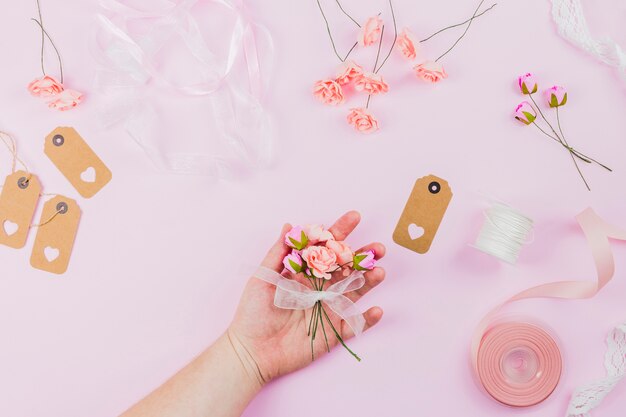 Nahaufnahme der Hand der Frau Blume halten gebunden mit weißem Band gegen rosa Hintergrund