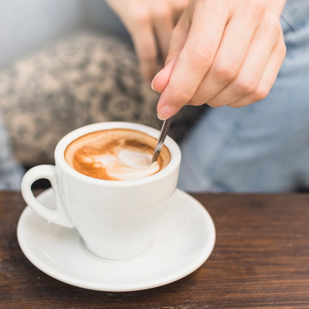 Nahaufnahme der Hand der Frau, die Kaffee Latte mit Löffel rührt