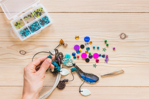 Nahaufnahme der Hand der Person, die handgemachten Schmuck auf Holztisch macht