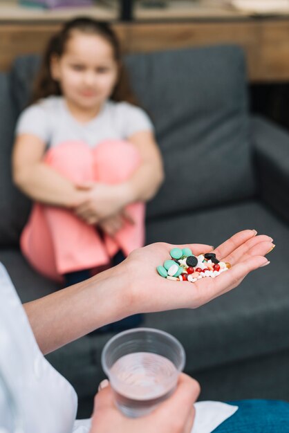 Nahaufnahme der Hand der Ärztin mit verschiedenen Pillen vor einem Mädchen, das auf Sofa sitzt