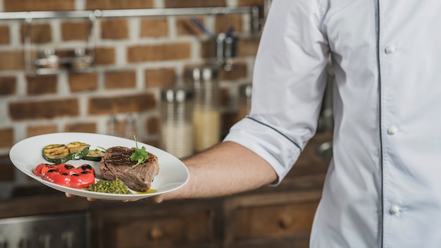 Nahaufnahme der Hand des männlichen Chefs, die in der Hand gebratenen Rindfleischteller hält