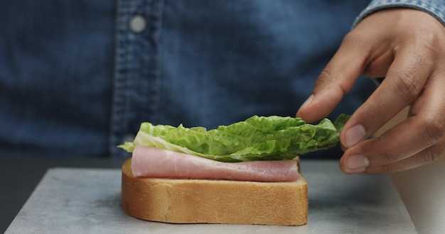 Nahaufnahme der Hand des Mannes, die Sandwich macht, legt von den Seiten alle Zutaten auf den Teller