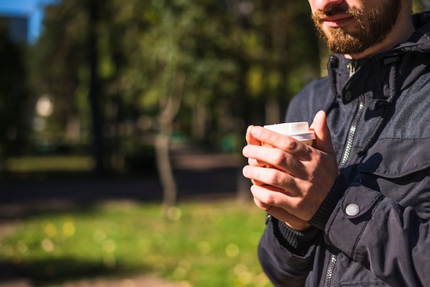 Nahaufnahme der Hand des Mannes Wegwerfkaffeetasse im Garten halten