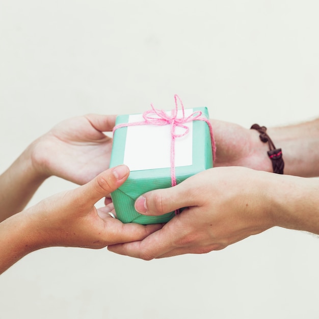 Nahaufnahme der Hand des Paares grüne Geschenkbox gegen normalen Hintergrund halten