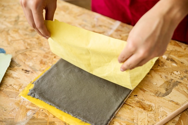 Nahaufnahme der Hand einer Frau, die gelbes Gewebe über Papiermasse hält