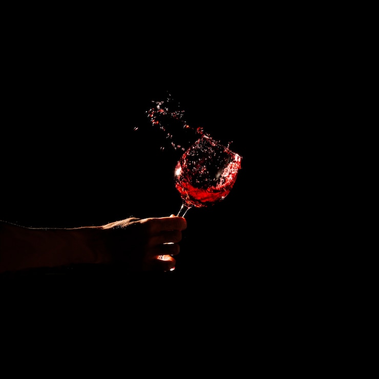 Kostenlose Foto nahaufnahme der hand einer person, die das glas rotwein spritzt aus glas hält
