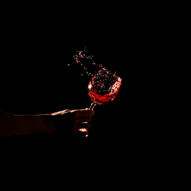 Nahaufnahme der Hand einer Person, die das Glas Rotwein spritzt aus Glas hält