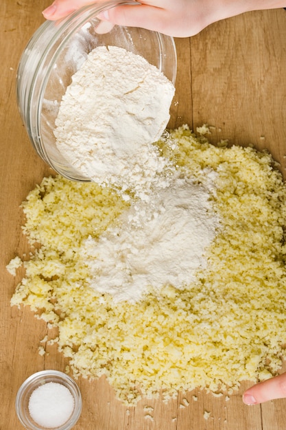 Nahaufnahme der Hand einer Person, die das Mehl in geriebenen Käse für das Zubereiten des italienischen Gnocchi gießt