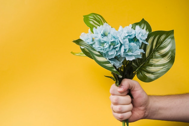 Nahaufnahme der Hand einer Person, die gefälschte Blume gegen gelben Hintergrund hält