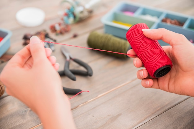 Nahaufnahme der Hand einer Person, die rote Garnrolle auf hölzernem Schreibtisch hält