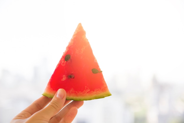 Nahaufnahme der Hand einer Person, die rote saftige dreieckige Wassermelonenscheibe im Sonnenlicht hält
