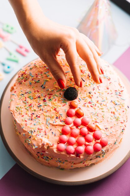 Nahaufnahme der Hand einer Person, die Schokoladenball auf verziertem Kuchen hält